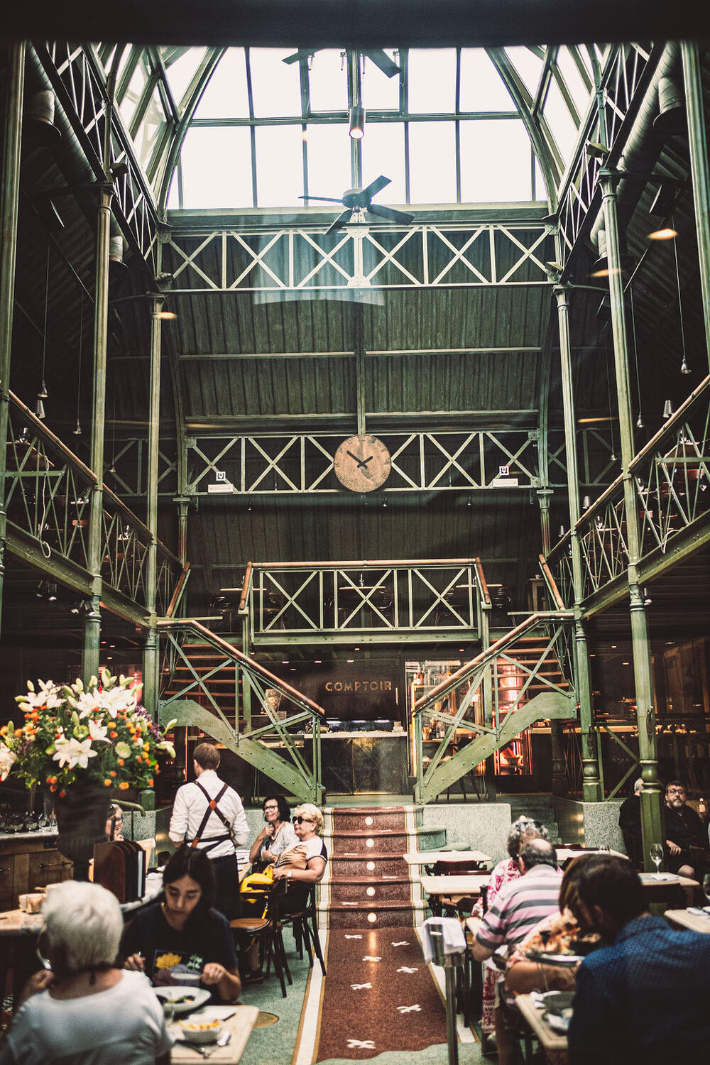 The restored 1880s warehouse interior of Pakhuis: exposed iron beams beneath a high glass roof, a long curved bar, warm wood floor.