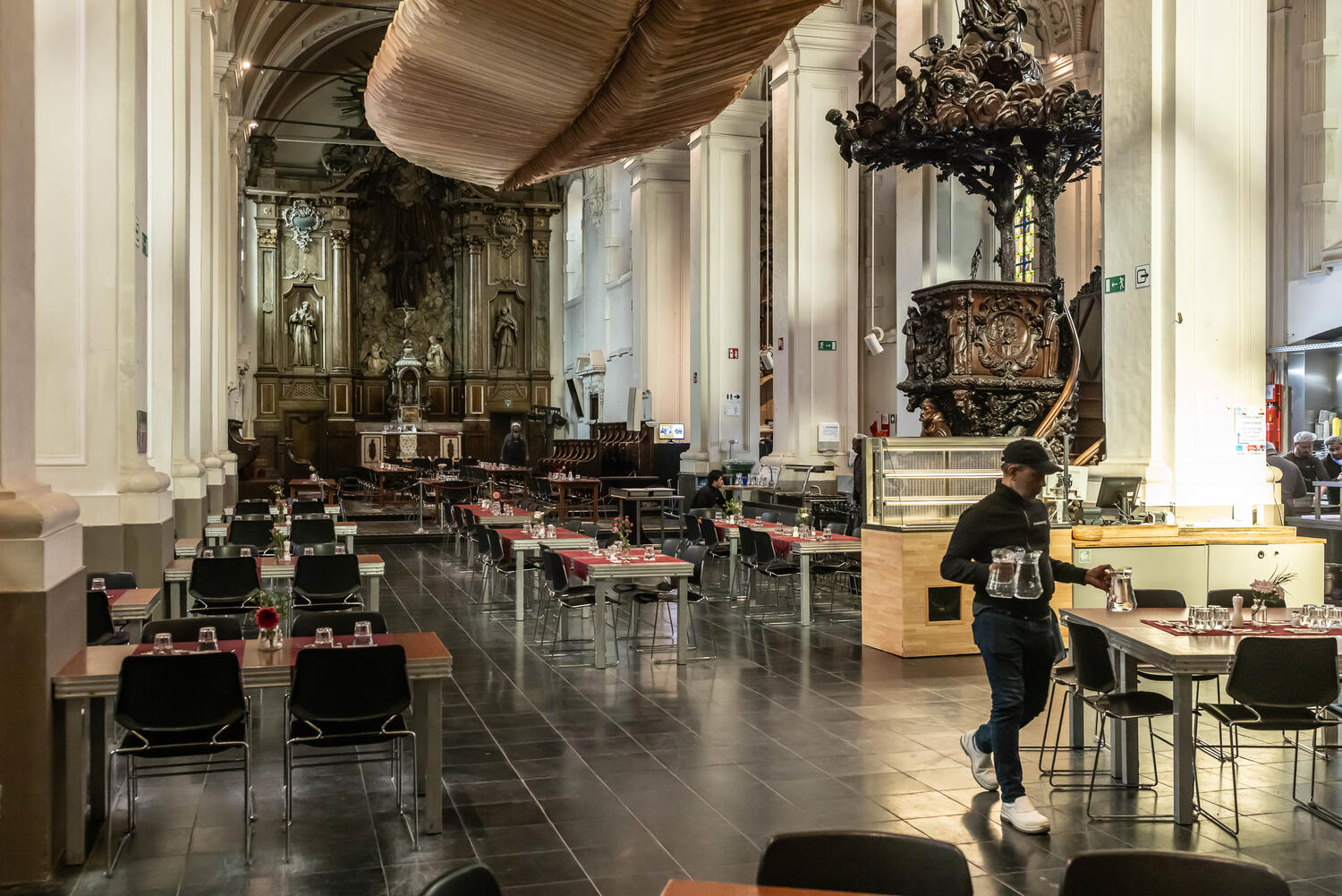 Lunch tables set inside the converted Franciscan church Parnassus, with original wooden benches and a new wooden structure dropping light from high in the nave.