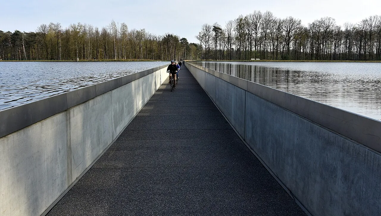 The Fietsen door het Water dyke path with cyclists riding at water level through a Bokrijk pond.