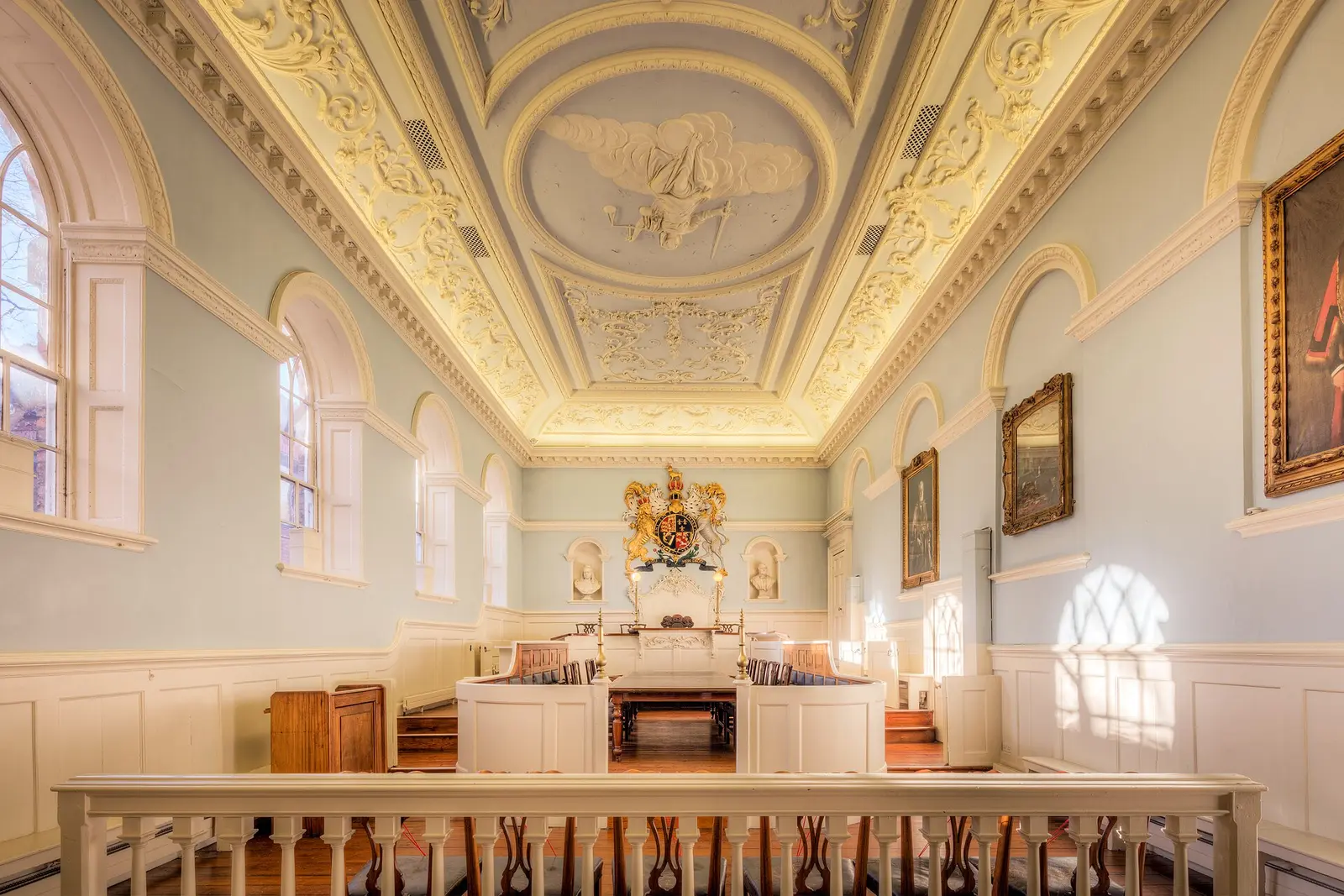 An empty panelled courtroom, benches and judge's seat under a decorated ceiling