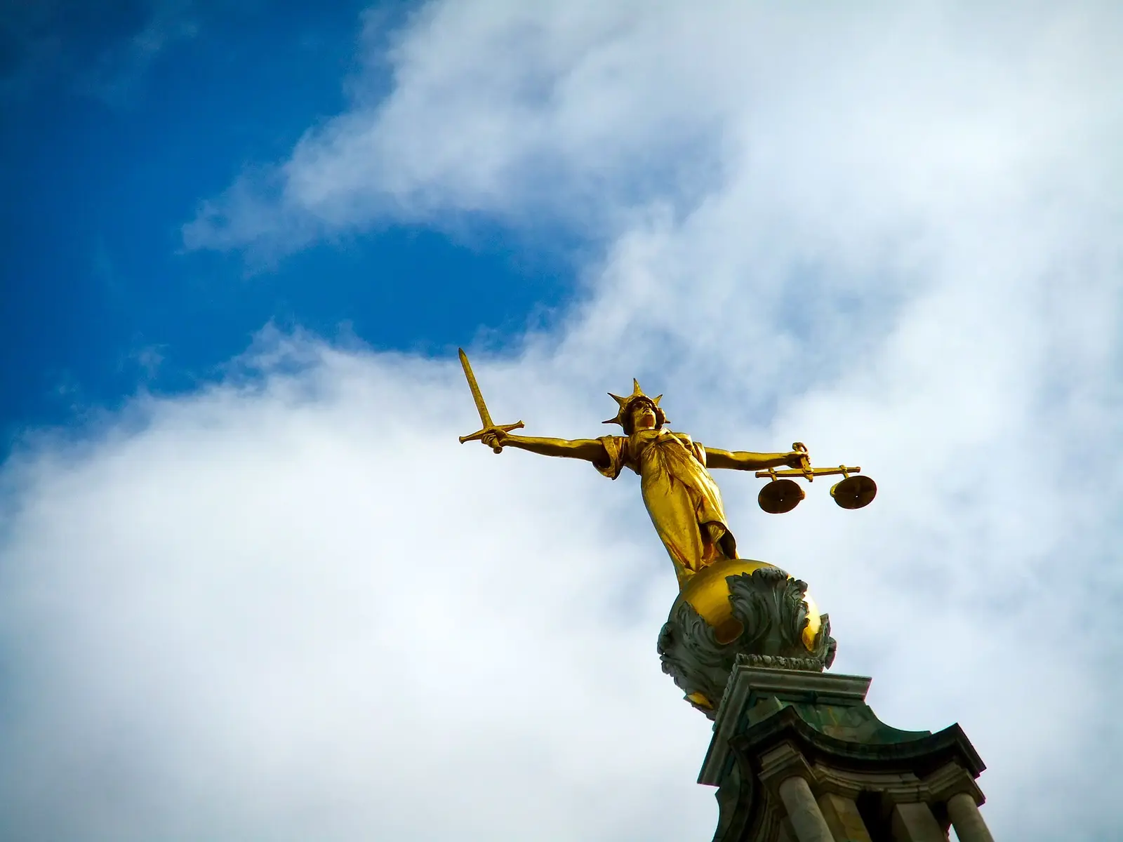 A bronze scales-of-justice sculpture against the sky