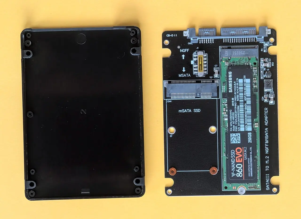 An M.2 SSD on an adapter board beside a 2.5-inch enclosure shell